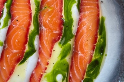 Un chef en tablier marron croise les bras devant un plan de travail dans une cuisine moderne.