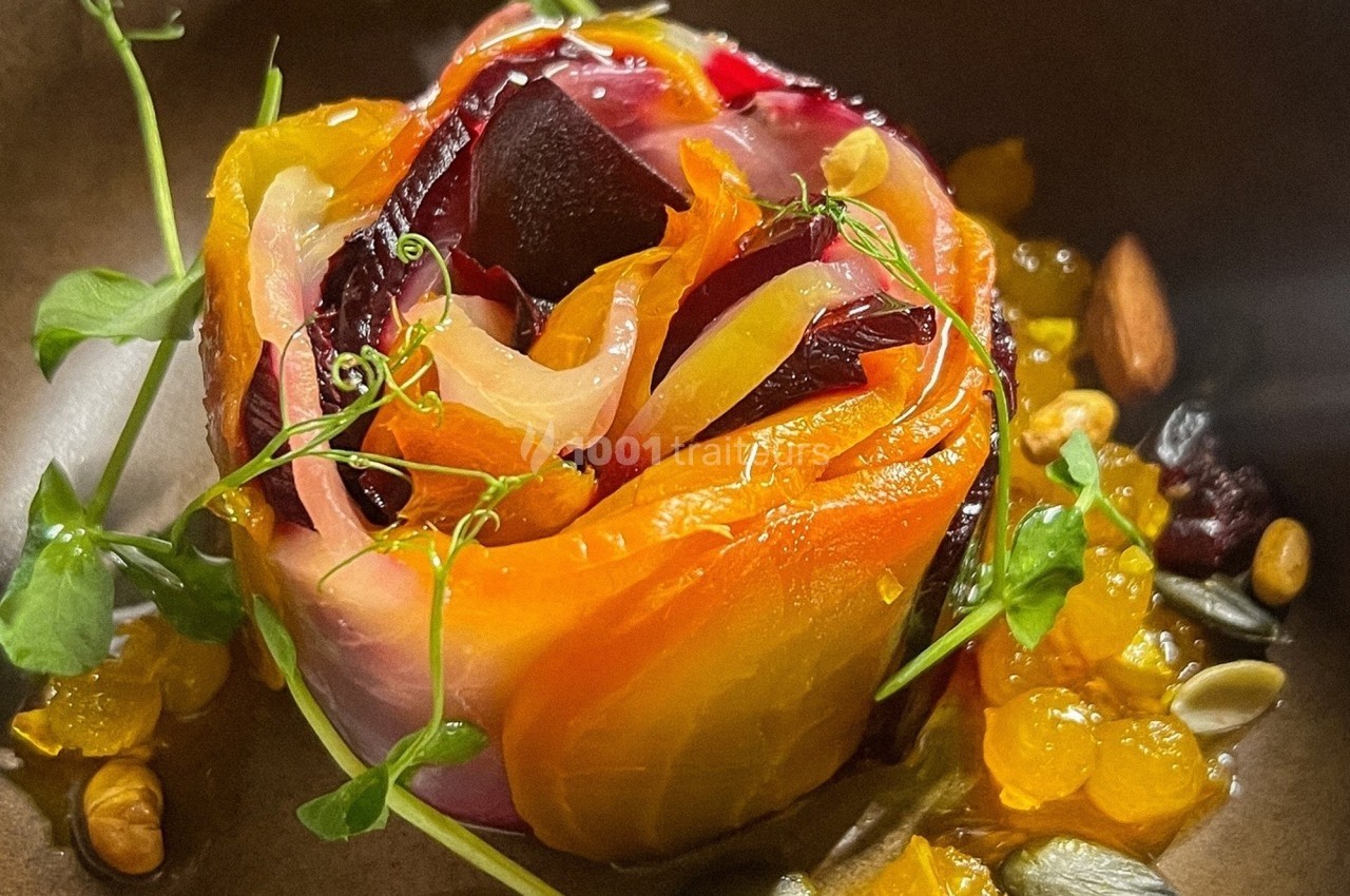 Assiette contenant une rose comestible faite de légumes colorés, garnie de graines, herbes fraîches et condiments.