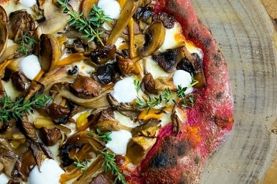 Un chef en tablier marron croise les bras devant un plan de travail dans une cuisine moderne.