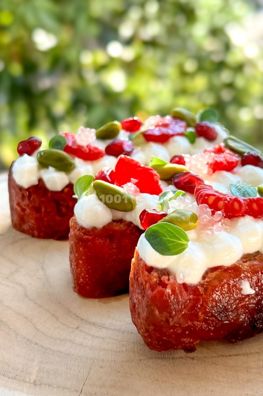 Tranches de brioche garnies de crème, graines, fruits rouges et pistaches, présentées sur une planche en bois.