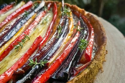 Un chef en tablier marron croise les bras devant un plan de travail dans une cuisine moderne.