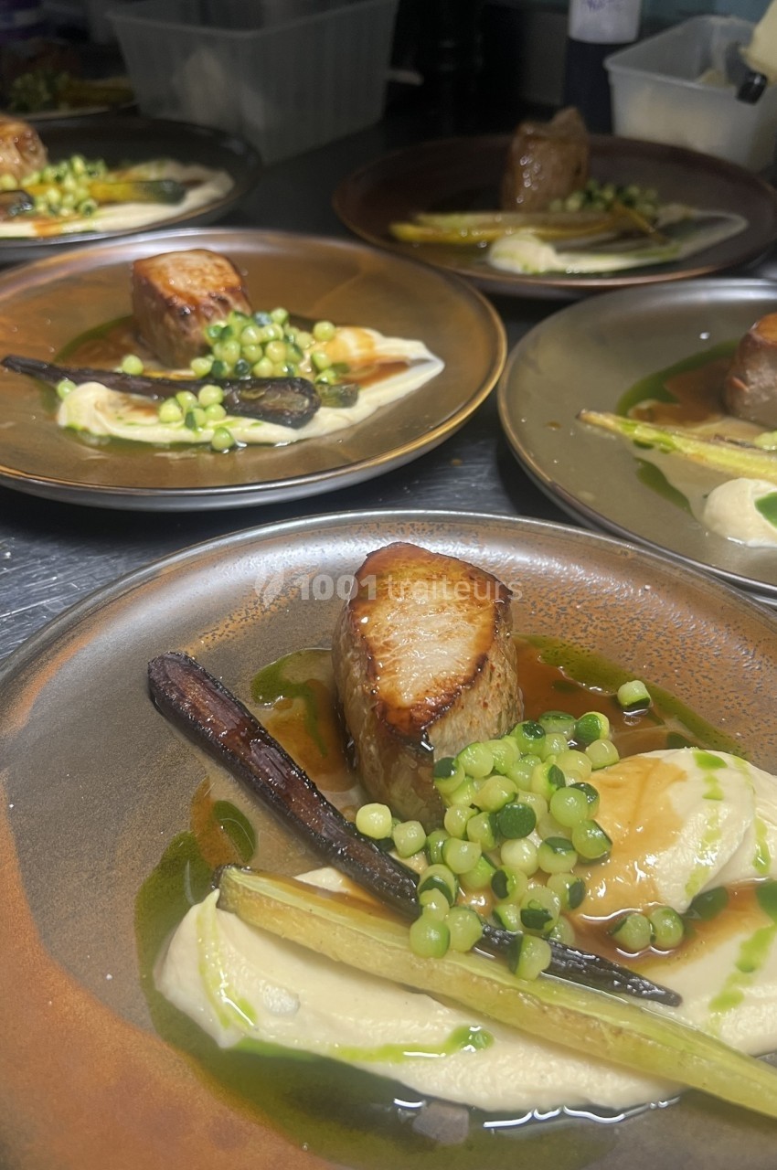 Assiette gastronomique avec viande grillée, purée, légumes verts, carotte et sauce, servie sur une table de cuisine.