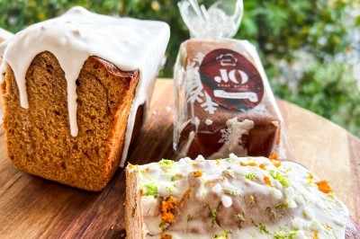 Un chef en tablier marron croise les bras devant un plan de travail dans une cuisine moderne.