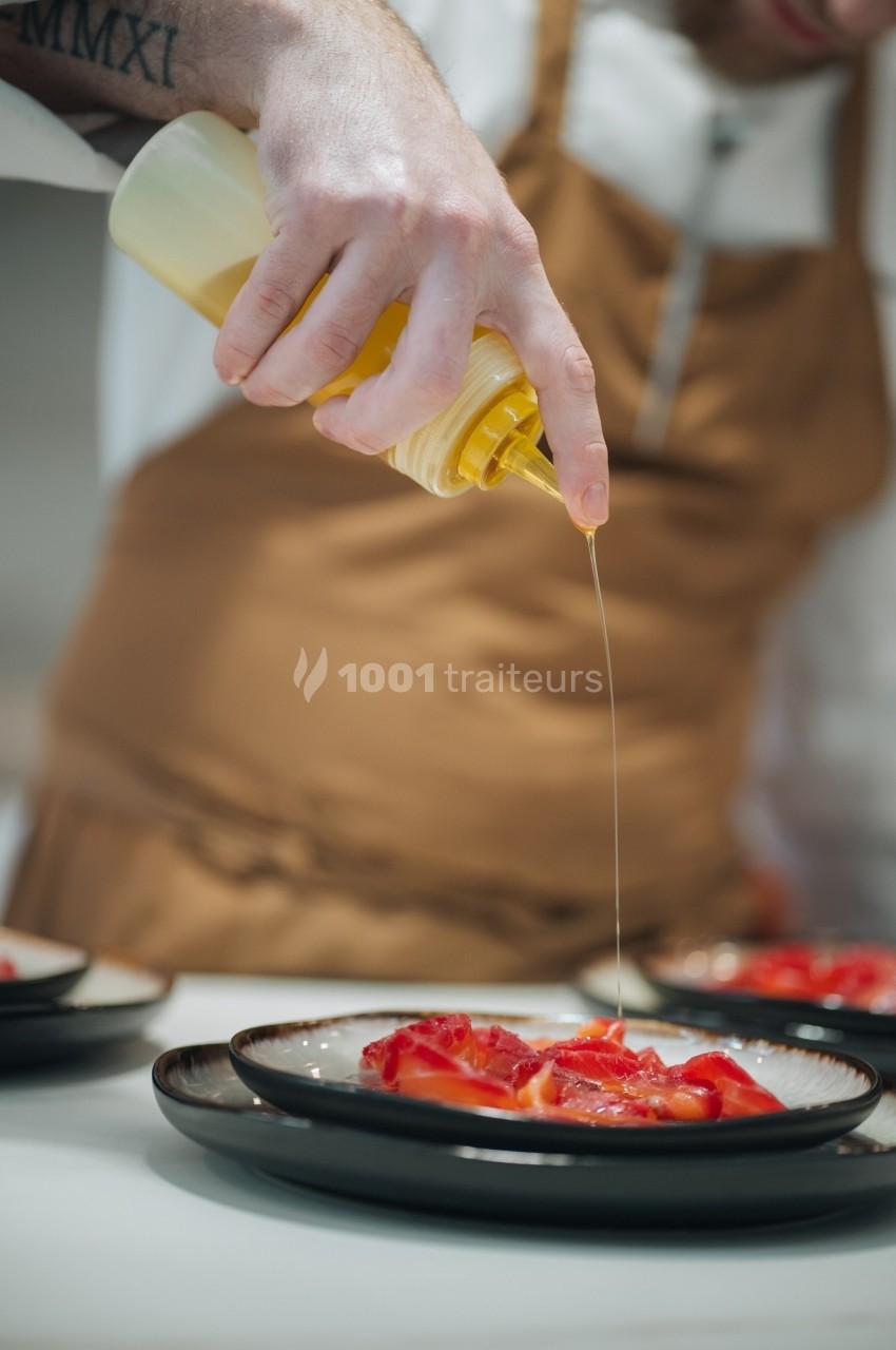 Un chef verse de l'huile sur un plat de légumes rouges disposés sur une assiette noire.
