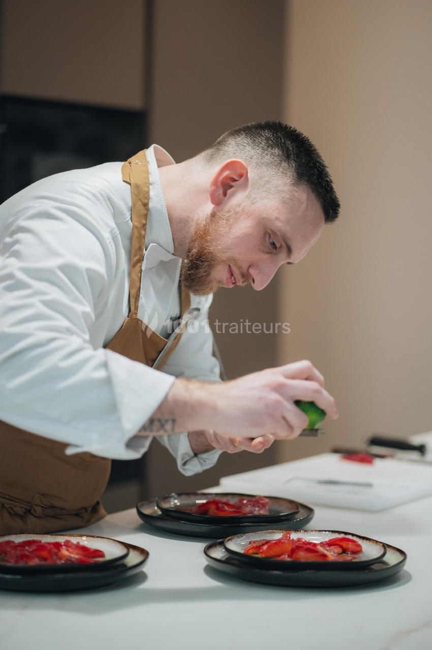 Un chef en tablier prépare des assiettes garnies de tranches de poisson cru dans une cuisine moderne.