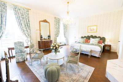 Chambre lumineuse avec lit double, parquet, rideaux orange, lustre et grandes fenêtres donnant sur l'extérieur.