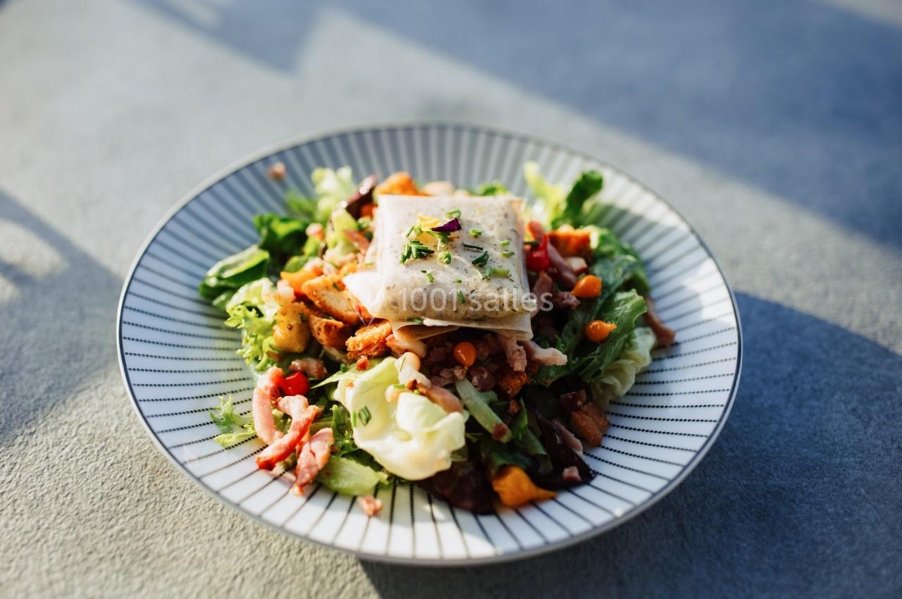 Assiette de salade garnie de légumes, lardons, croûtons et d'un carré de fromage fondu, servie sur une table.