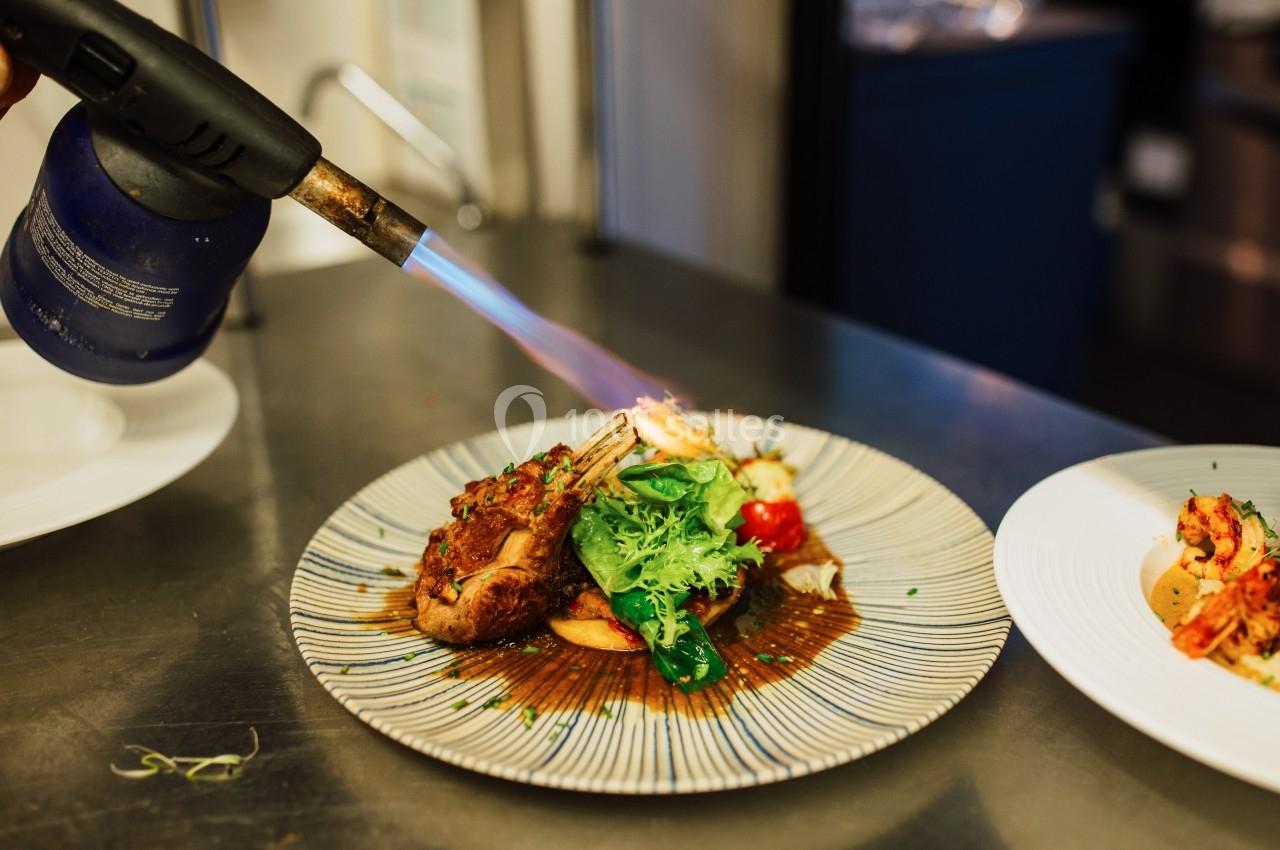Un chef caramélise un plat de viande et légumes avec un chalumeau dans une cuisine professionnelle.