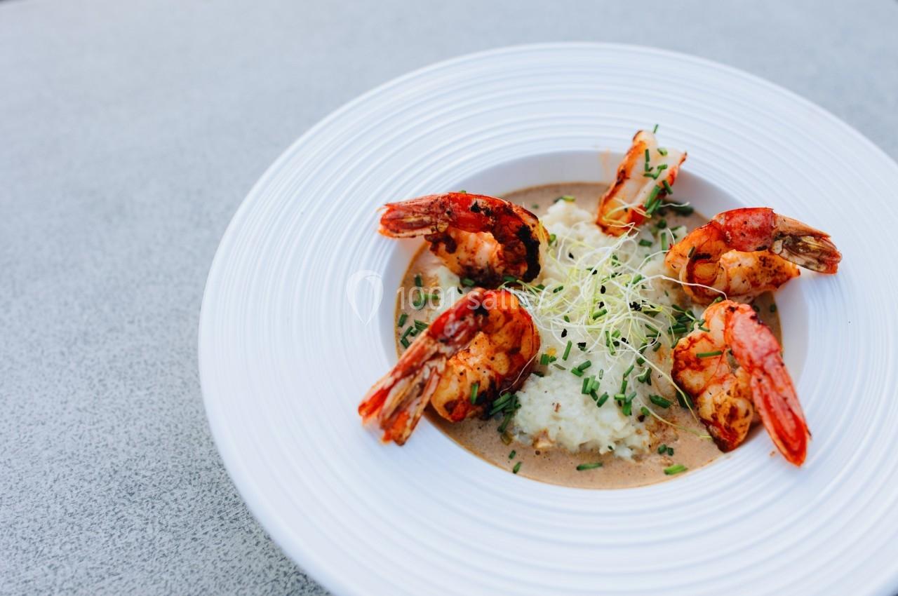 Assiette de crevettes grillées servies avec une purée et des pousses fraîches, présentée sur une table grise.