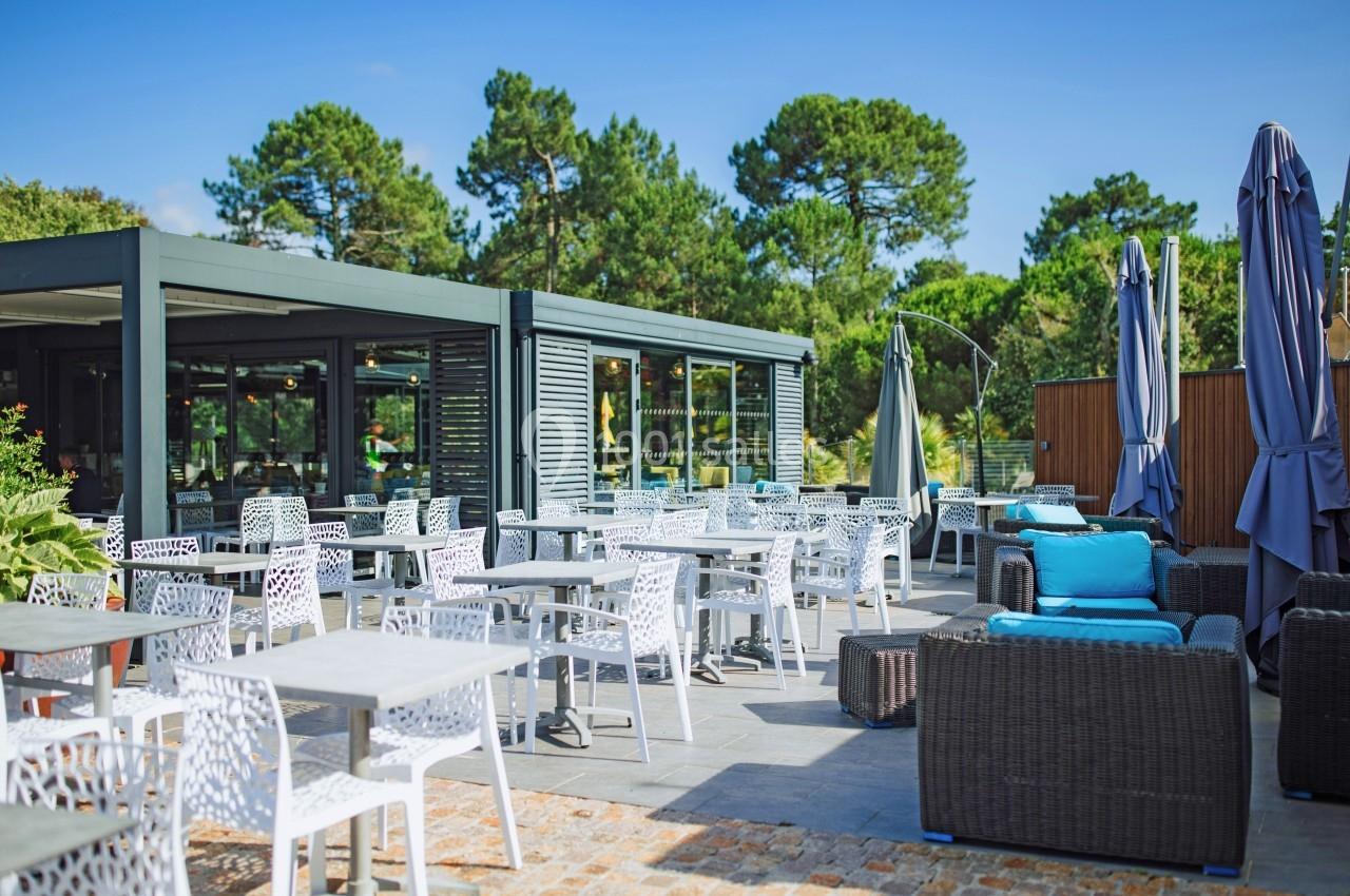 Terrasse extérieure d'un restaurant avec tables, chaises blanches et mobilier en rotin sous un ciel dégagé.
