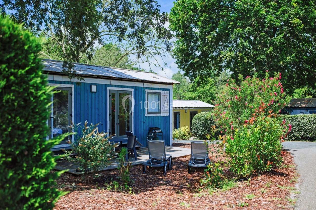 Chalet bleu avec terrasse aménagée, entouré de végétation et situé dans un cadre arboré par temps ensoleillé.