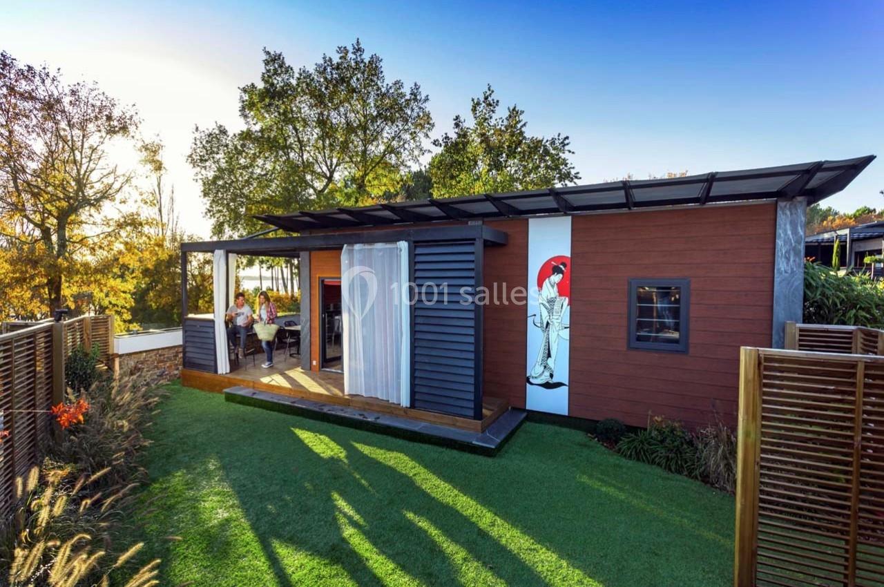 Maison en bois moderne avec terrasse, grandes baies vitrées et jardin verdoyant sous un ciel dégagé.