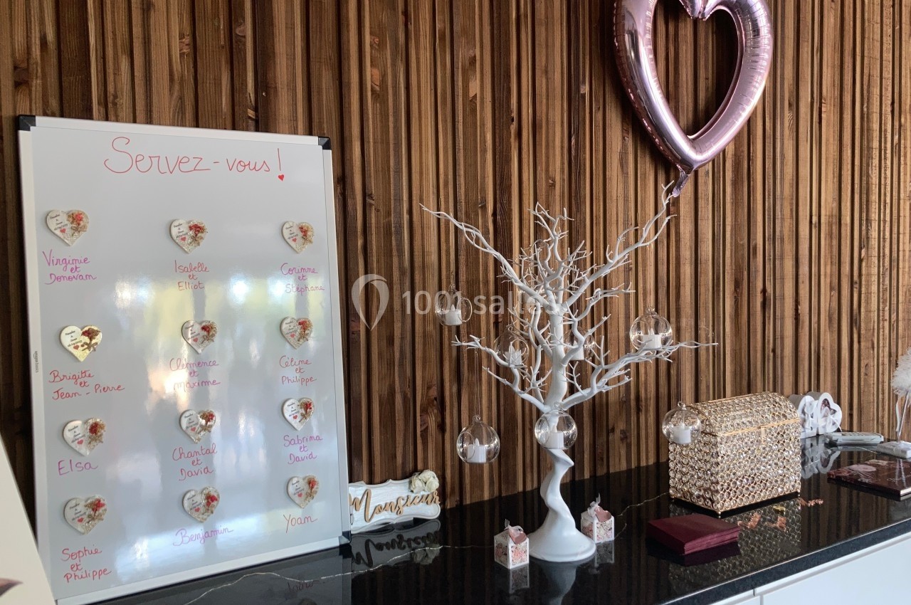 Table décorative avec un tableau de noms, un arbre blanc orné de boules transparentes et un ballon en forme de cœur.