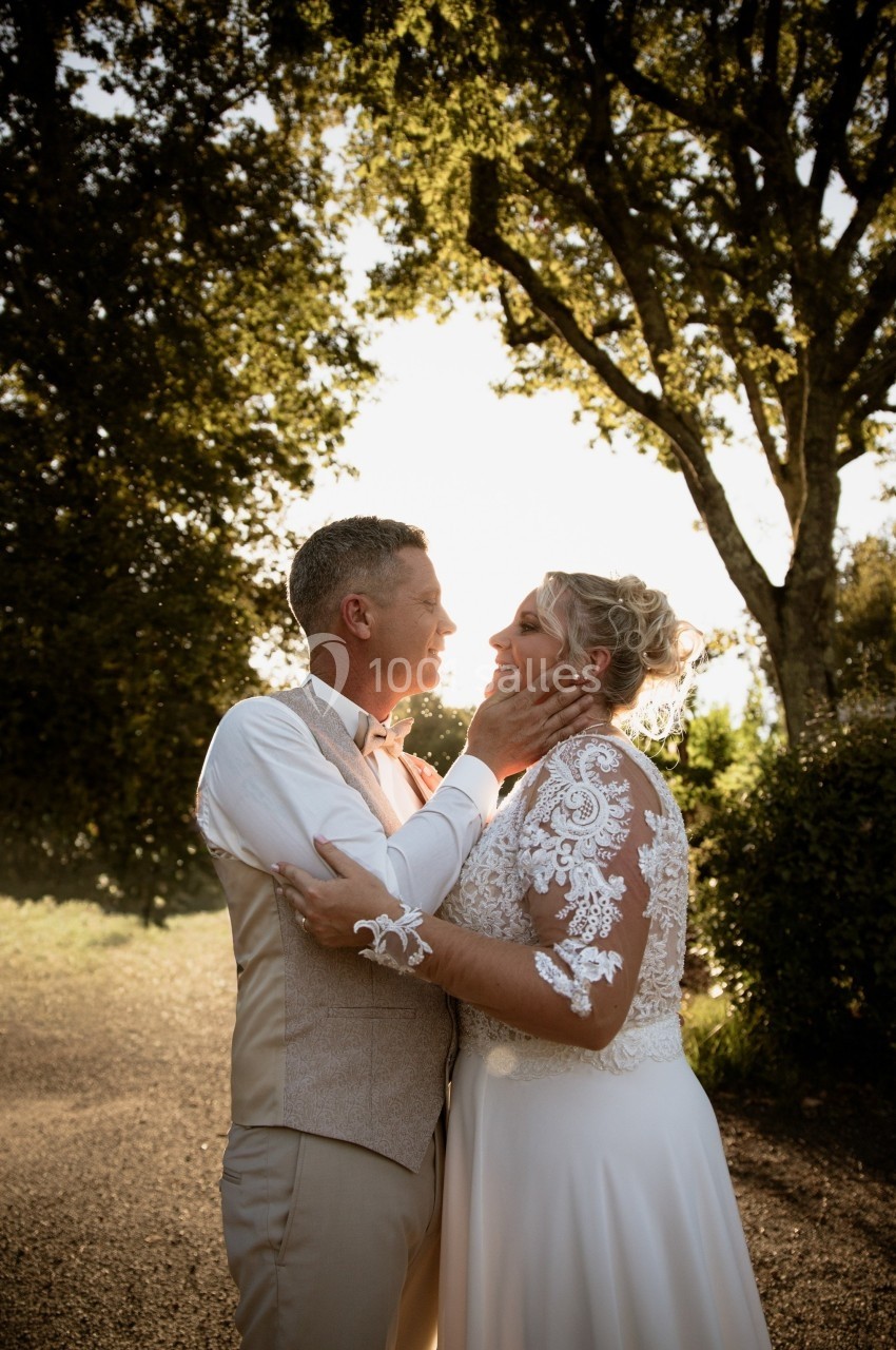 Un couple en tenue de mariage s'enlace tendrement dans un jardin au coucher du soleil.