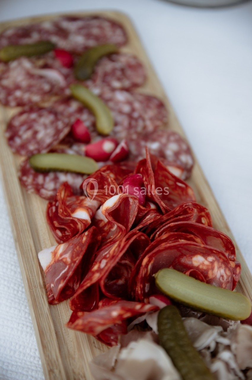 Plateau de charcuterie avec tranches de saucisson, cornichons et radis disposés sur une planche en bois.