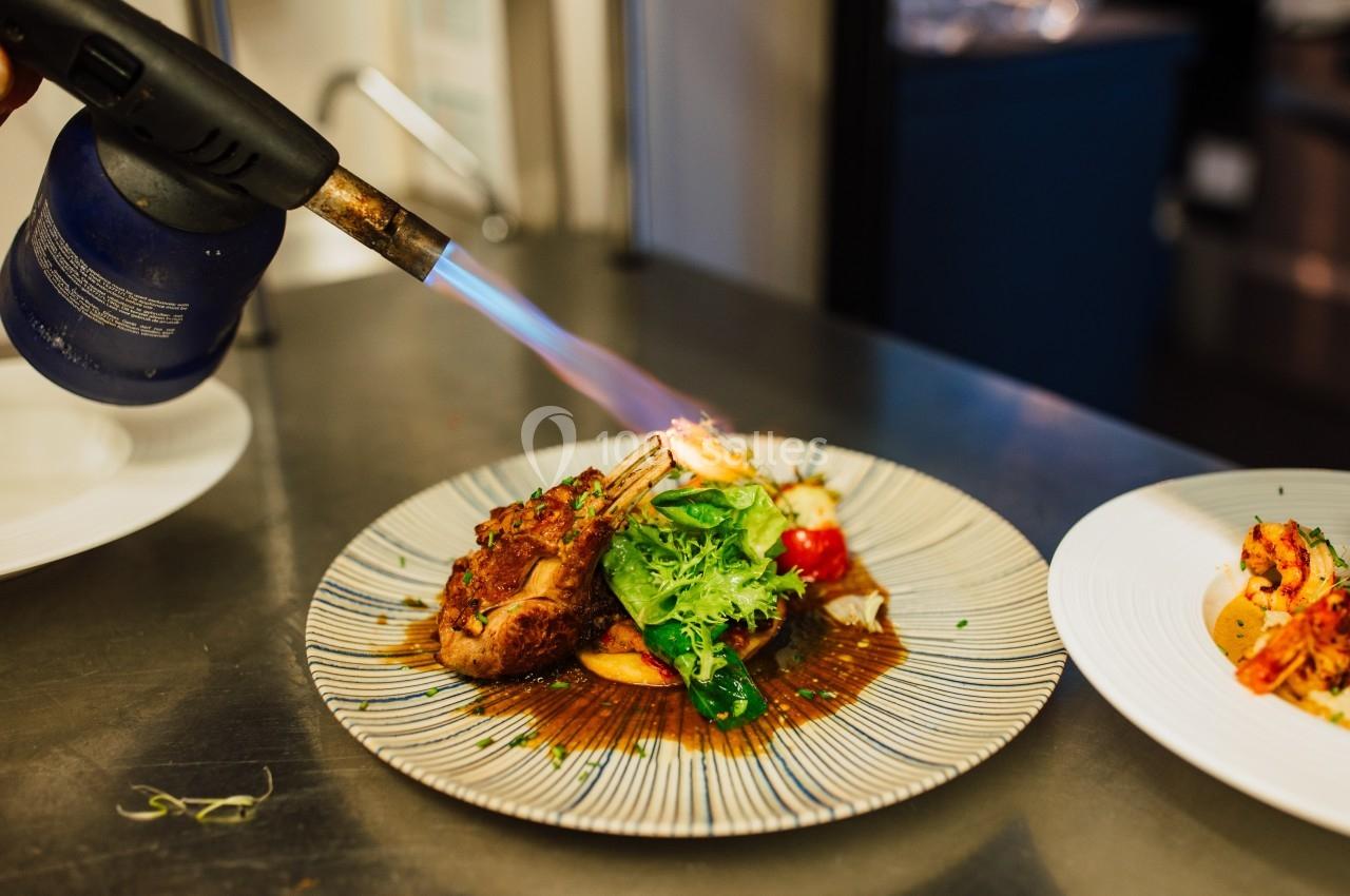 Un chef caramélise un plat de viande et légumes avec un chalumeau dans une cuisine professionnelle.