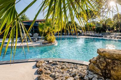 Vue aérienne d'un complexe avec piscines, bâtiments, espaces verts et parkings, entouré de végétation.