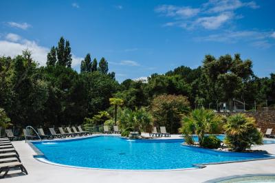 Vue aérienne d'un complexe avec piscines, bâtiments, espaces verts et parkings, entouré de végétation.