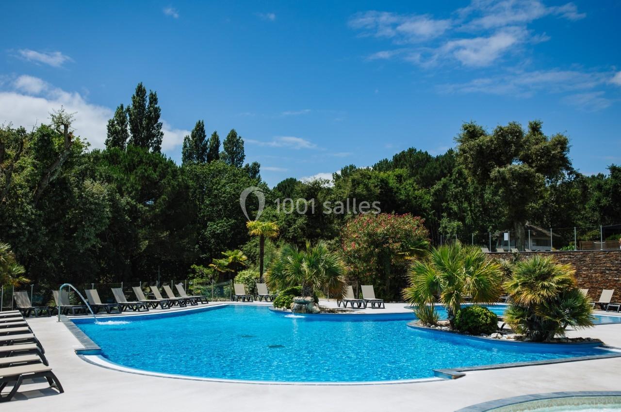 Piscine extérieure entourée de chaises longues, palmiers et végétation luxuriante sous un ciel bleu.