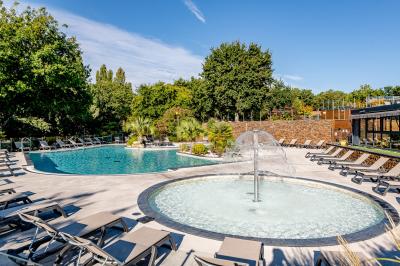 Vue aérienne d'un complexe avec piscines, bâtiments, espaces verts et parkings, entouré de végétation.