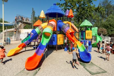 Un enfant avec des brassards orange glisse sur un toboggan rouge dans une piscine extérieure ensoleillée.