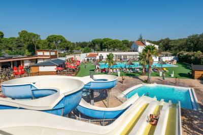 Un enfant avec des brassards orange glisse sur un toboggan rouge dans une piscine extérieure ensoleillée.