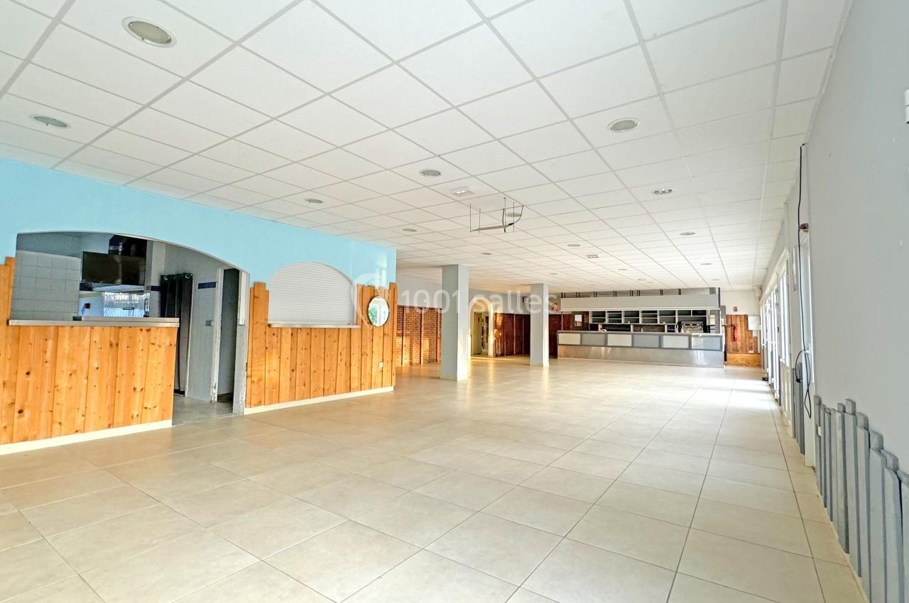 Salle spacieuse avec carrelage clair, murs en bois et peinture bleue, comptoir et cuisine visibles au fond.