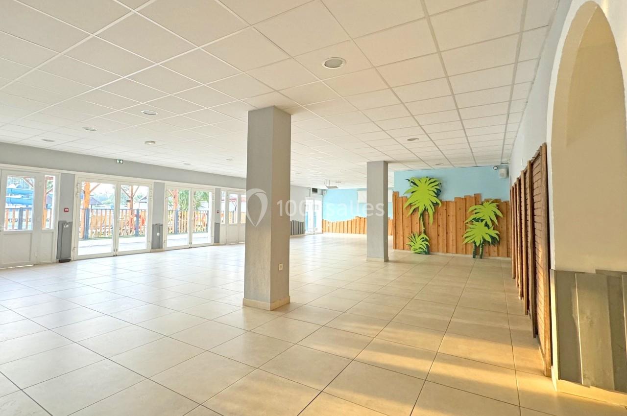 Salle lumineuse avec carrelage clair, murs blancs et décorations murales en forme de palmiers près d'une cloison en bois.