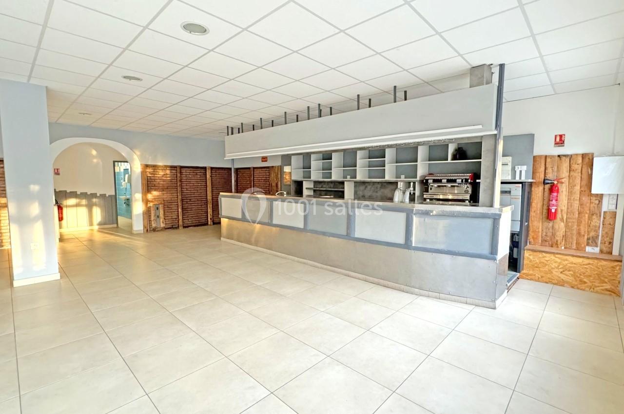 Intérieur d'un espace lumineux avec comptoir en métal, murs en briques et carrelage clair au sol.