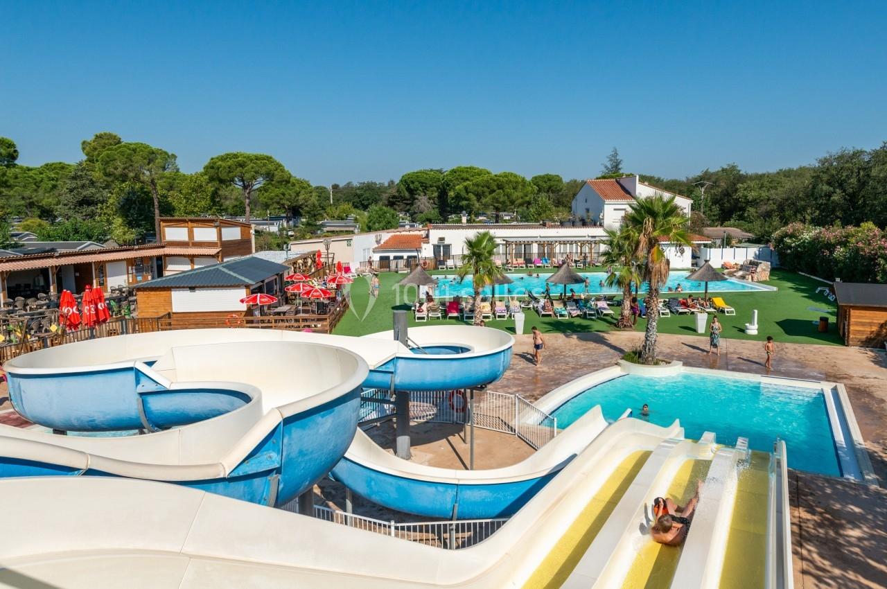 Vue d'un parc aquatique avec toboggans, piscine, transats et espaces verts sous un ciel dégagé.