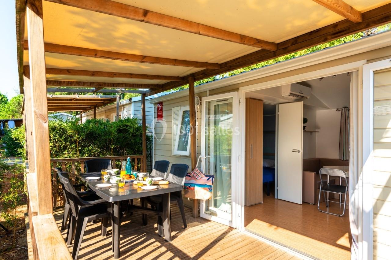 Terrasse en bois aménagée avec table et chaises, attenante à un mobil-home lumineux avec porte coulissante ouverte.