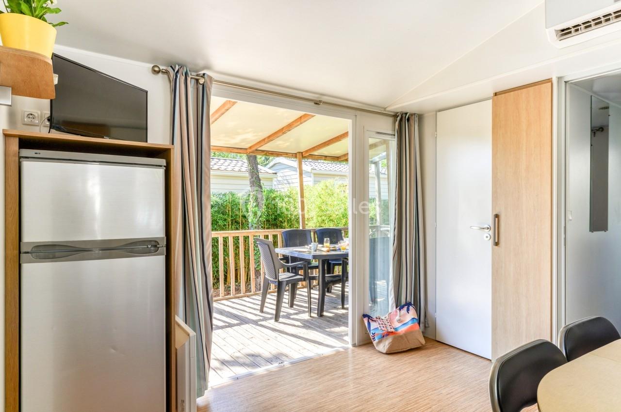 Intérieur lumineux avec vue sur une terrasse en bois aménagée, table et chaises extérieures visibles à travers une baie…