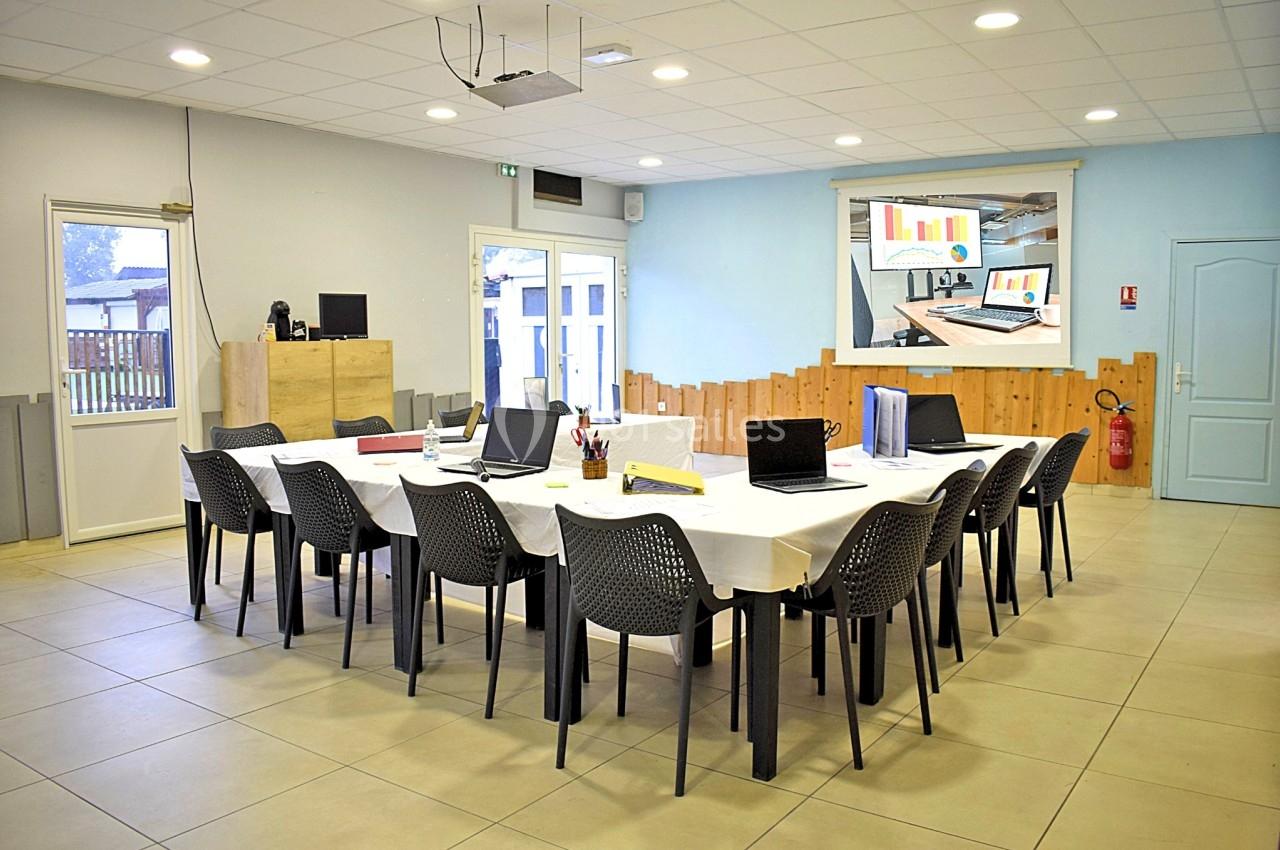 Salle de réunion équipée de tables en U, chaises, ordinateurs portables et écran de projection affichant des graphiques.