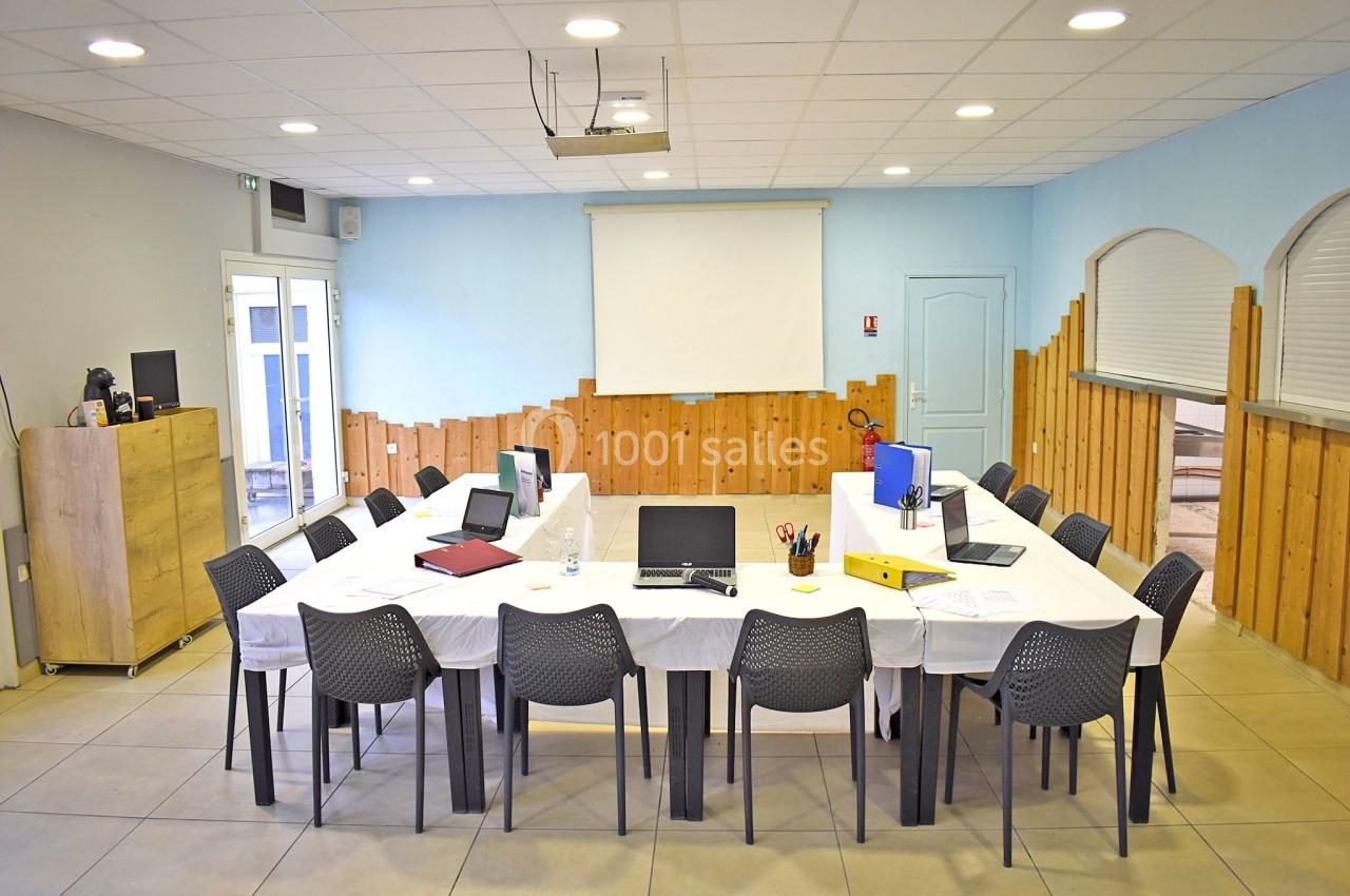 Salle de réunion équipée avec une grande table rectangulaire, des chaises, des ordinateurs et un projecteur.