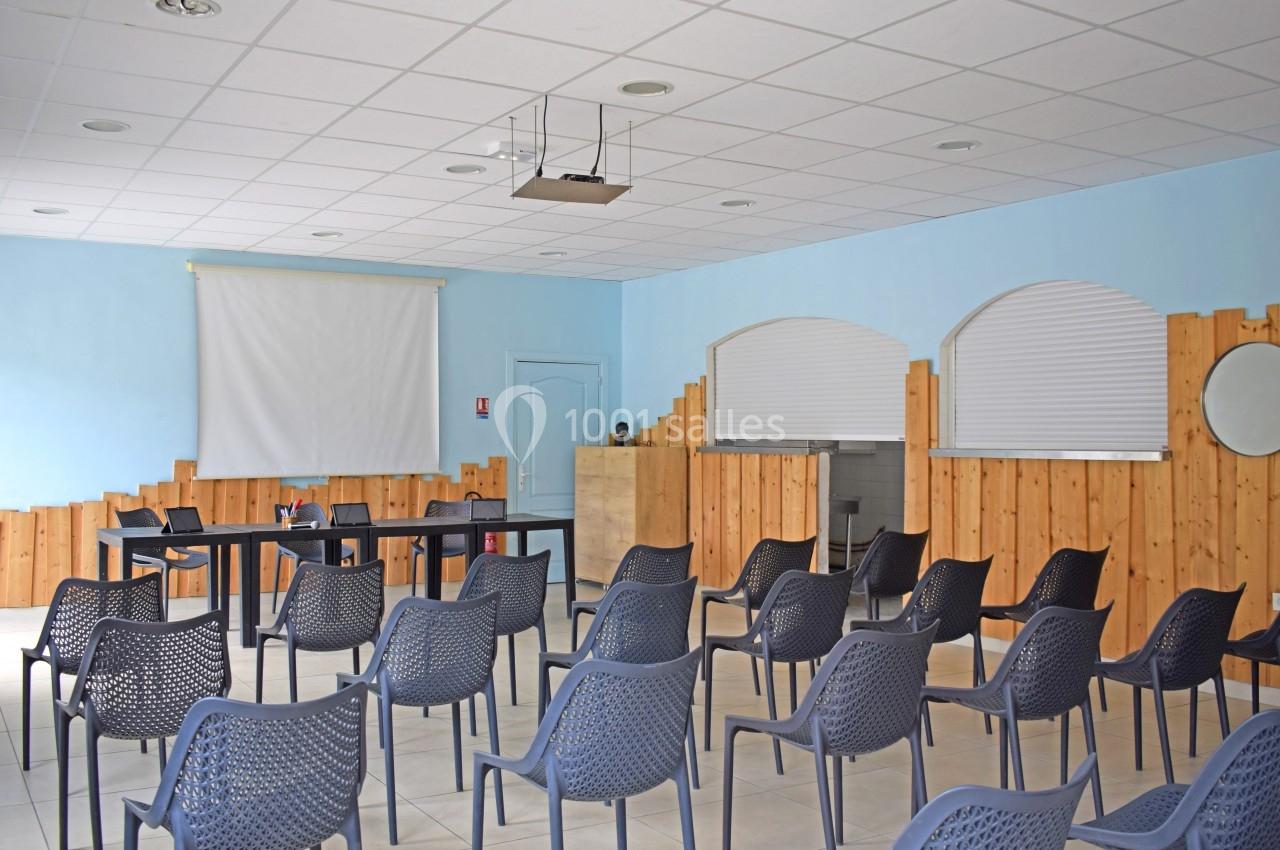 Salle de réunion avec des chaises en plastique noir disposées face à un écran de projection et une table.