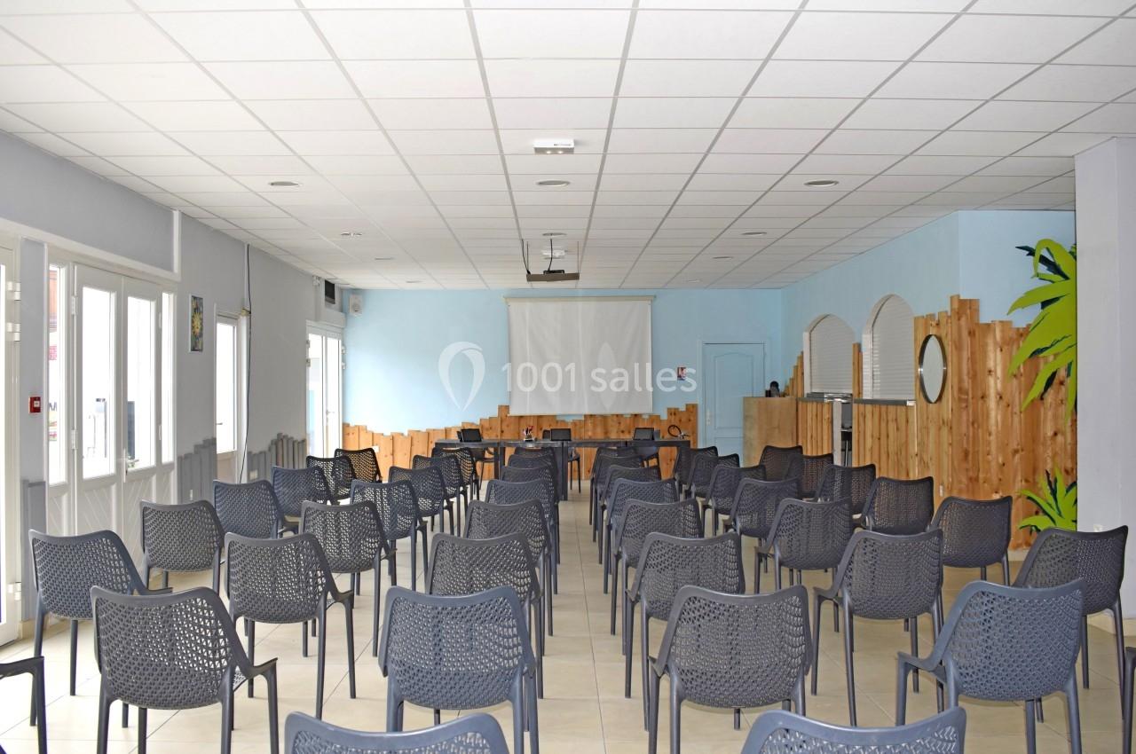 Salle lumineuse avec des rangées de chaises en plastique noir, un écran de projection et des murs décorés de bois clair.