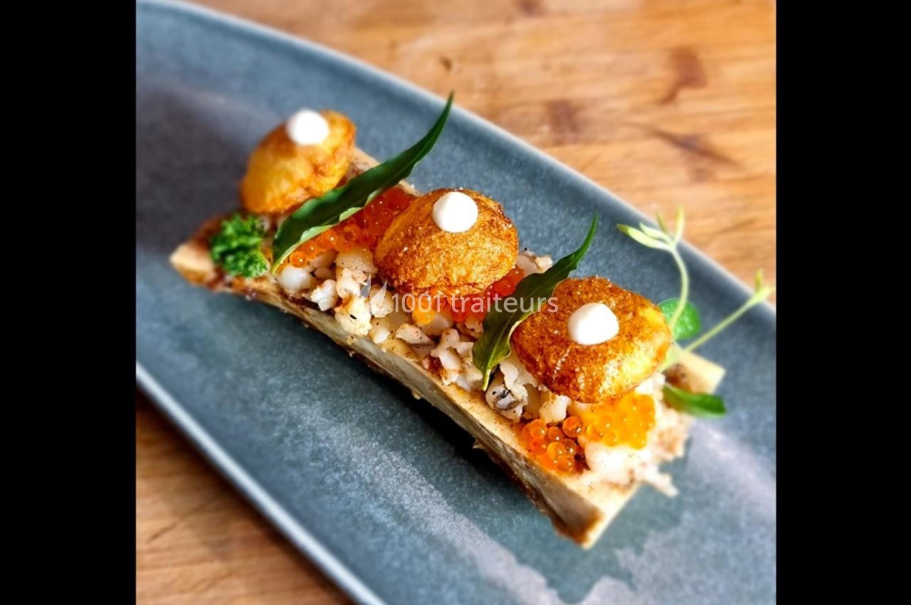 Os à moelle garni de caviar, oursins, herbes fraîches et crème, présenté sur une assiette en céramique bleue.