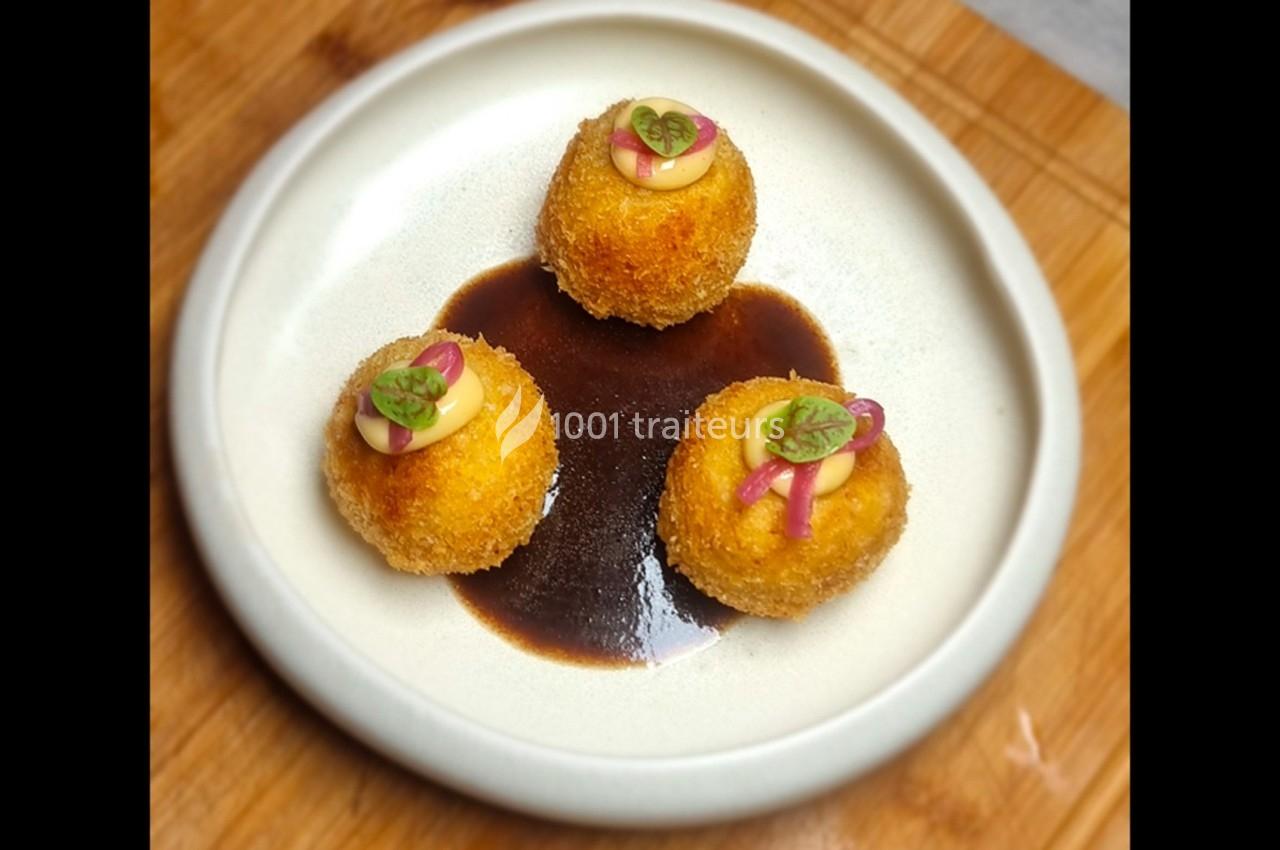 Trois croquettes dorées garnies de mayonnaise, oignons rouges et herbes, servies sur une sauce brune.