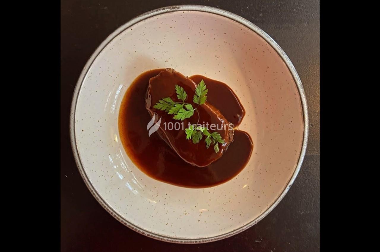 Plat de viande nappé de sauce brune, garni de feuilles de persil, présenté dans une assiette blanche.