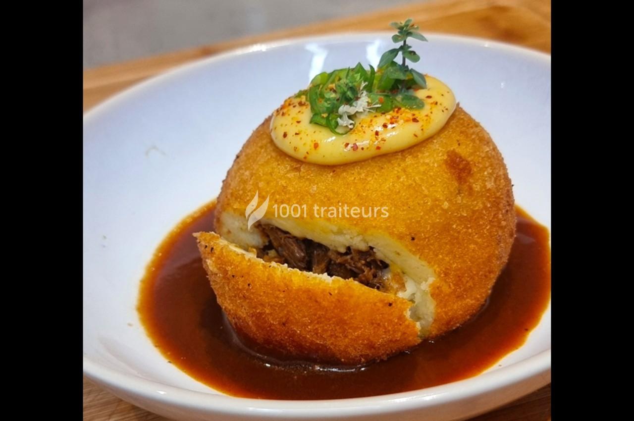 Boule de purée panée garnie de viande effilochée, servie avec une sauce brune et une garniture crémeuse.