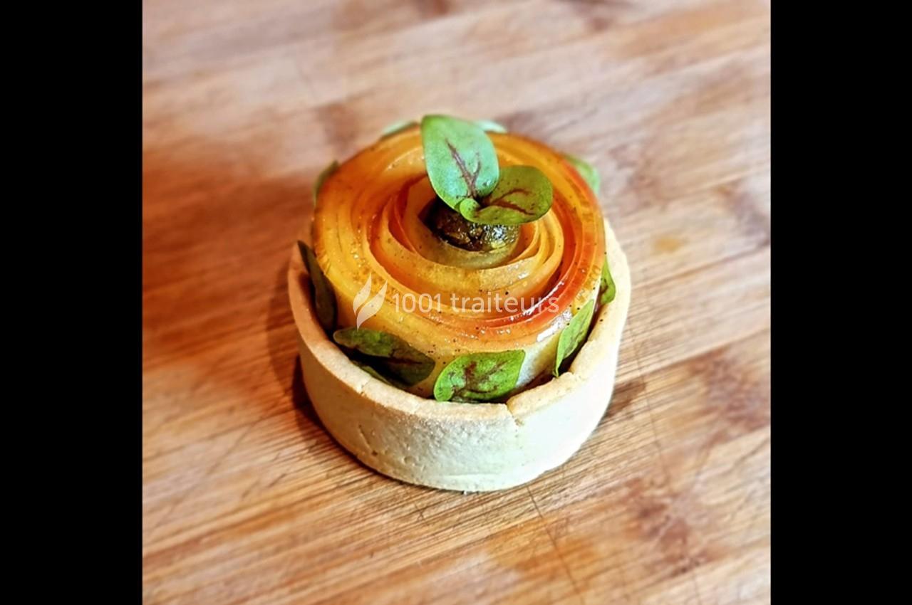 Tartelette garnie de fines tranches de fruits disposées en spirale, décorée de feuilles vertes sur une planche en bois.