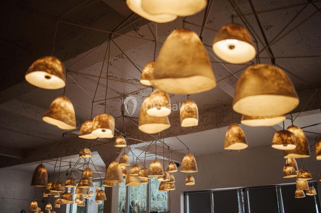 Suspensions lumineuses en papier beige accrochées au plafond d'une pièce avec des fenêtres en arrière-plan.