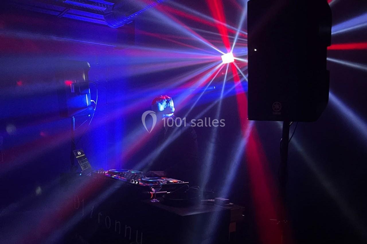 Un DJ mixe dans une ambiance sombre avec des jeux de lumière colorés et des faisceaux rouges et bleus.