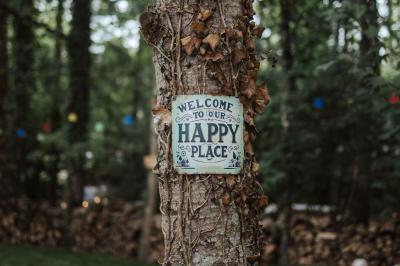 Panneau ’Welcome to our happy place’ fixé à un arbre entouré de lierre dans une forêt.
