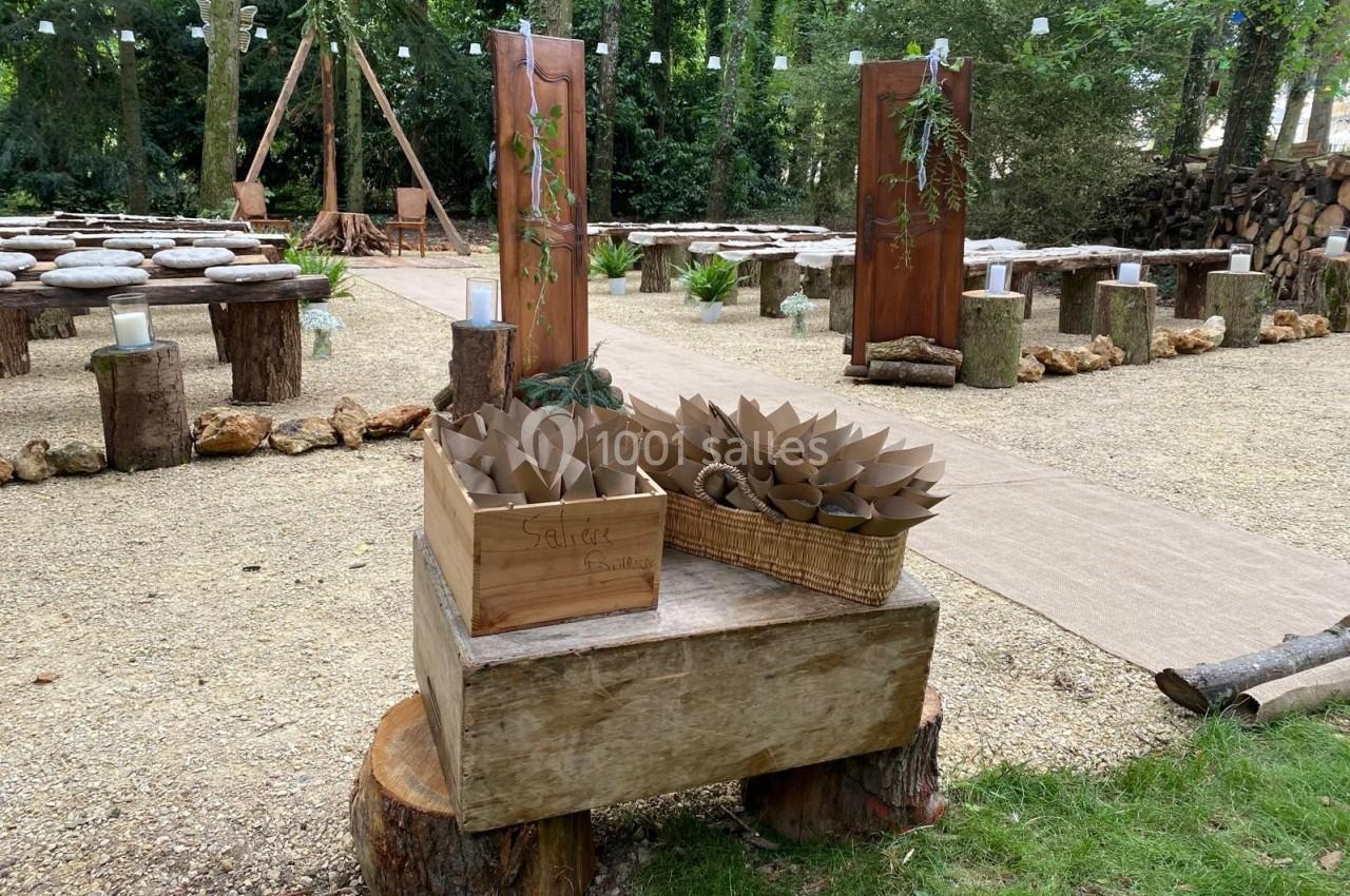Décor extérieur pour une cérémonie, avec allée centrale, chaises en rondins et paniers contenant des cônes en papier.