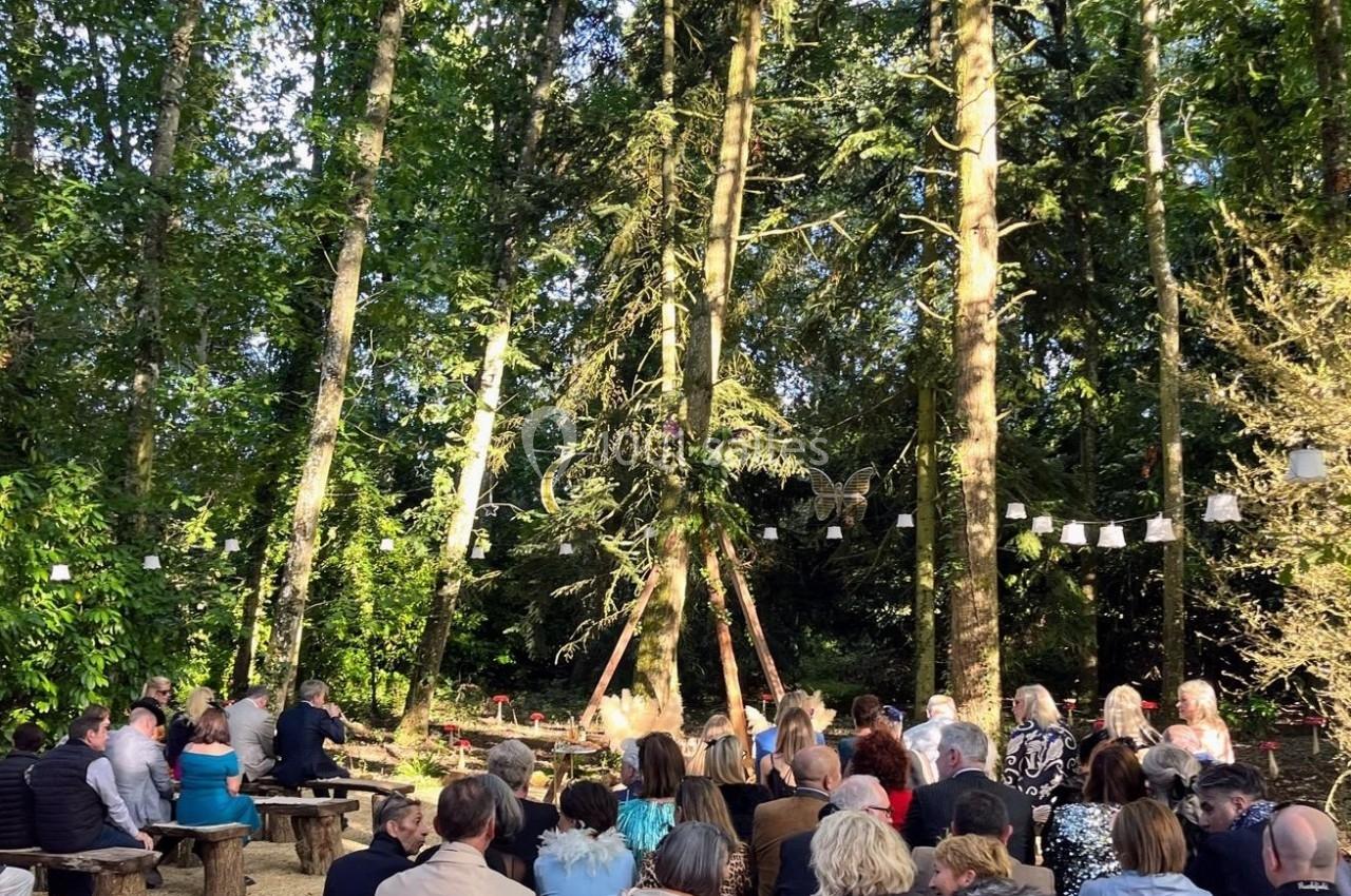 Groupe de personnes assises sur des bancs en bois dans une clairière entourée d'arbres, lors d'un événement en plein air.