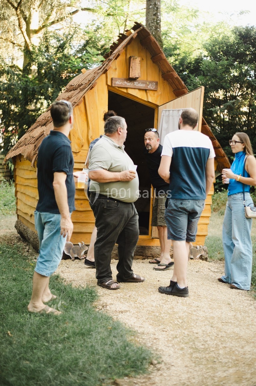 Un groupe de personnes discute devant une petite cabane en bois dans un cadre extérieur verdoyant.