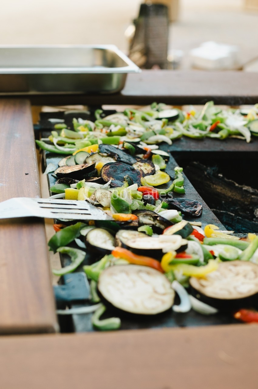 Légumes variés grillés sur une plancha en extérieur, avec une fourchette en métal au premier plan.