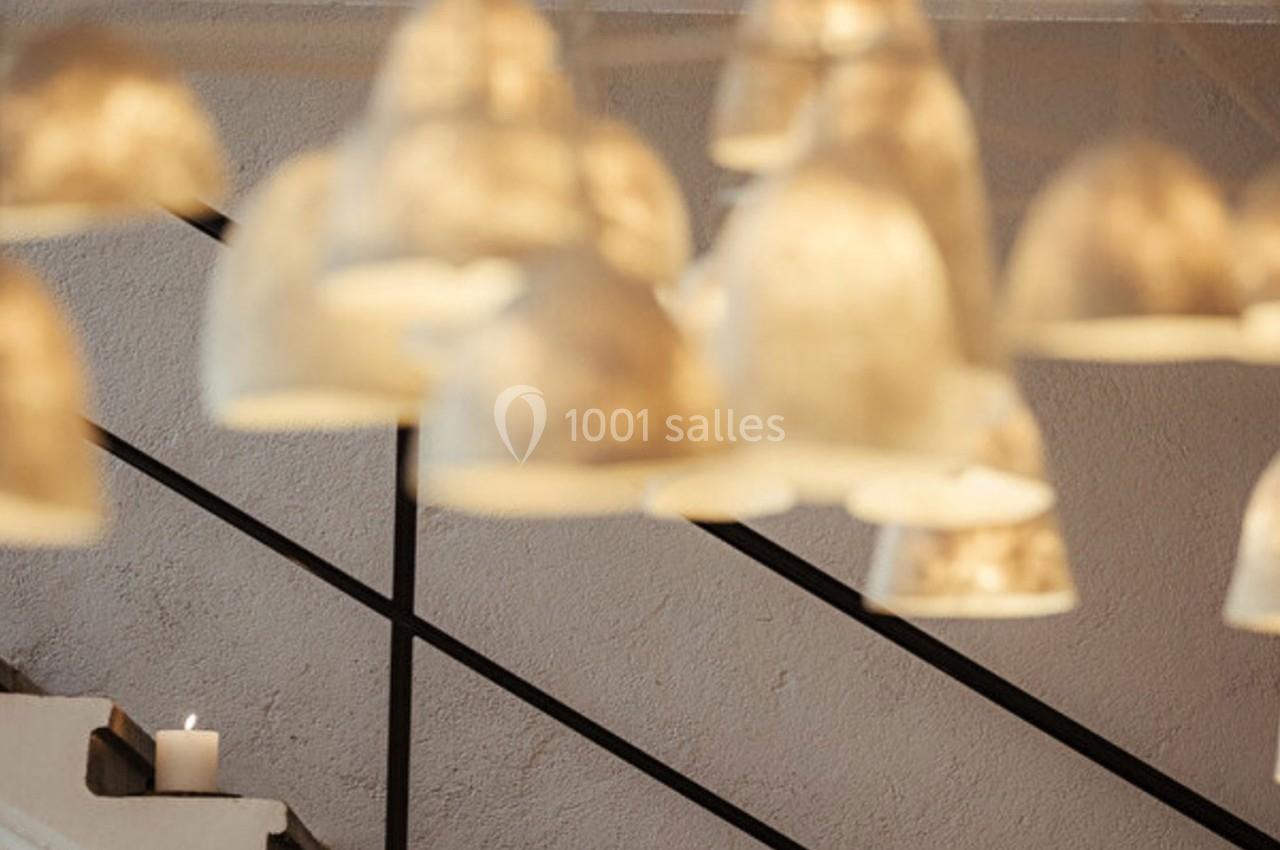 Suspensions lumineuses floues au premier plan, escalier en arrière-plan avec une bougie allumée sur une marche.