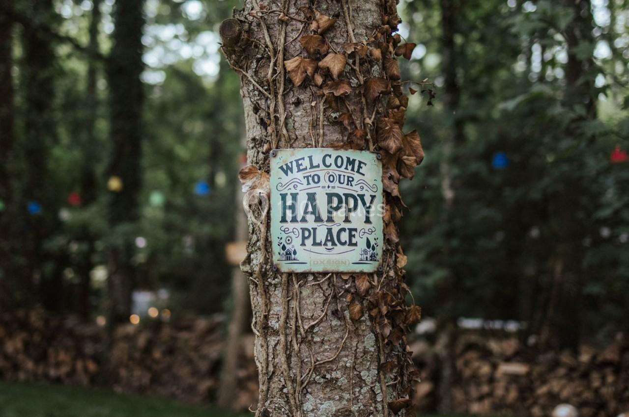 Panneau ’Welcome to our happy place’ fixé à un arbre entouré de lierre dans une forêt.